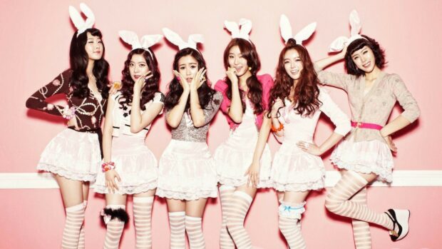 Six K pop idols posing with bunny ears in a playful pink themed photoshoot