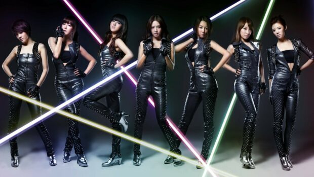 A K Pop girl group dressed in black leather outfits posing with colorful neon lights in the background