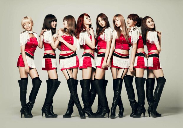 A K pop girl group wearing red and white outfits with black high boots posing together