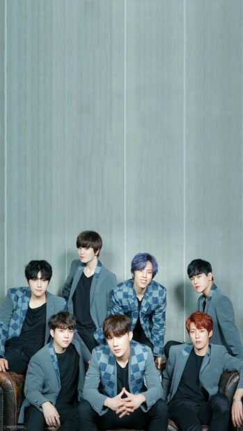 A K Pop group posing together in stylish suits against a blue wall