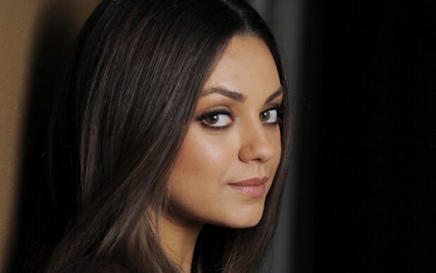 Mila Kunis posing with a serene expression and long dark hair against a dark background