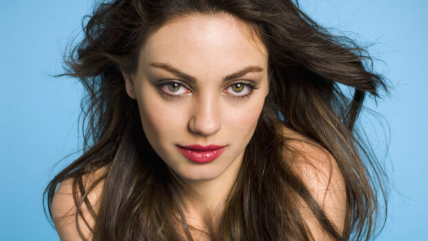 Mila Kunis with flowing hair and striking green eyes against a blue background