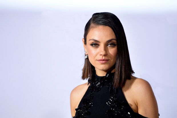 Mila Kunis in a black dress with short straight hair looking confidently at the camera