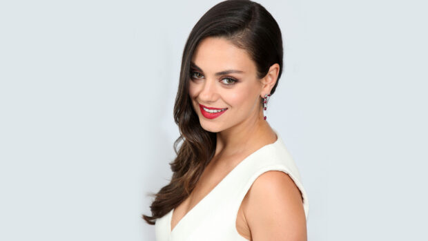 Mila Kunis with long dark hair and red lipstick smiling in a white outfit