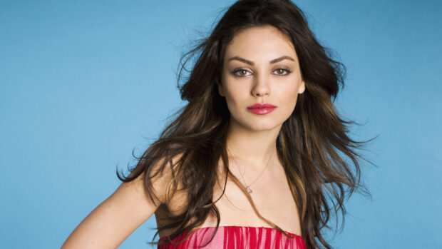 Mila Kunis wearing a red dress with flowing hair against a blue background