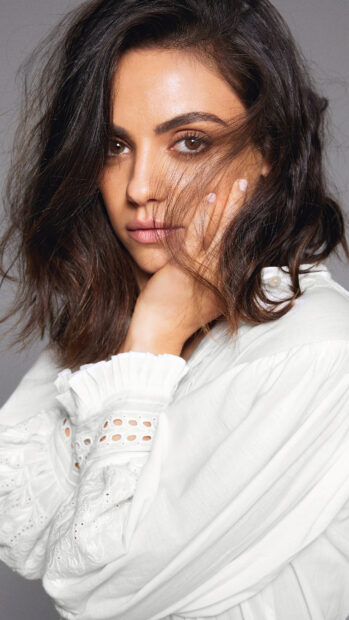 Mila Kunis with brown eyes and loose hair in a white blouse looking thoughtfully