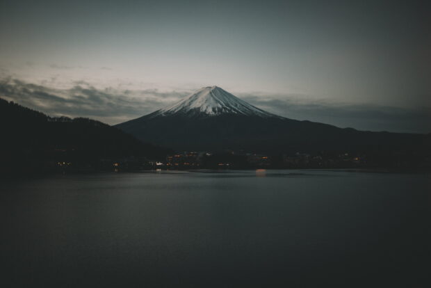 Snow capped Mount Fuji Japan at twilight with calm lake and city lights in foreground