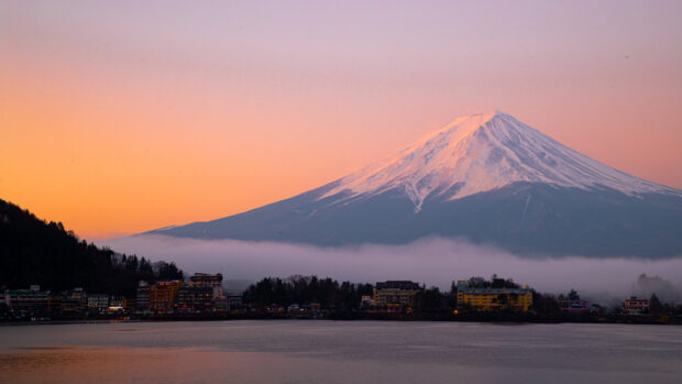 Snow capped Mount Fuji Japan with lakeside village under a colorful sunset sky