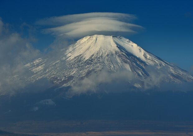 Snow covered Mount Fuji Japan with unique cloud formation in the clear sky