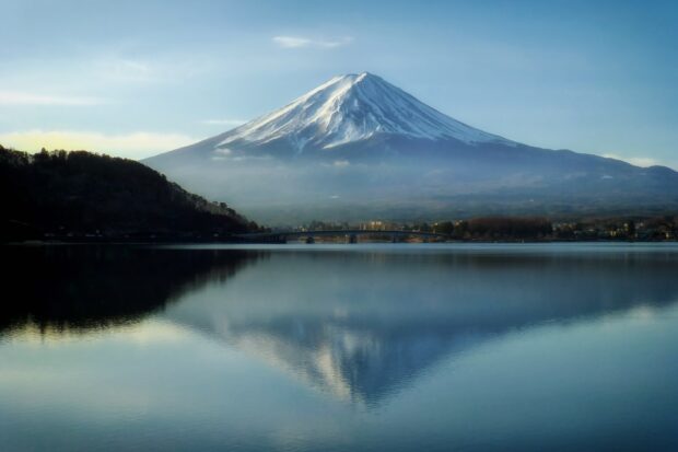 A clear view of Mount Fuji Japan reflected in calm lake water surrounded by forested hills