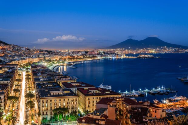 Nighttime cityscape of Naples with coastal views and Mount Vesuvius in the background