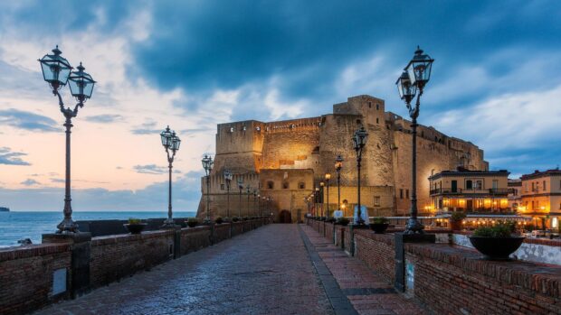 Ancient Naples castle and street lamps lining the pathway at sunset