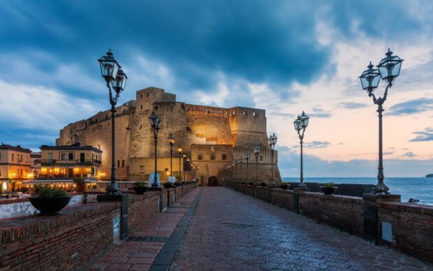 Historic castle in Naples illuminated at dusk with dramatic sky view
