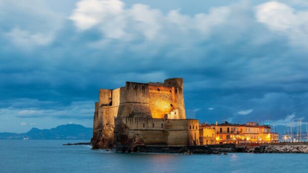 Historic fortress in Naples illuminated at dusk under cloudy sky