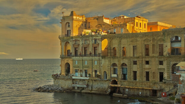 Historic stone building on Naples coast with sea and sky at sunset