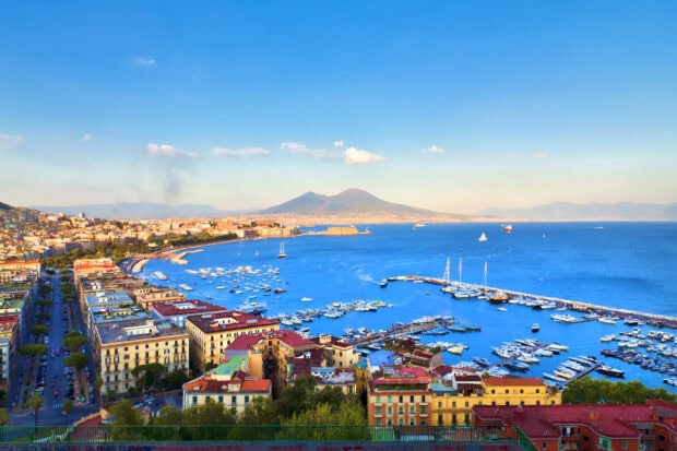 Panoramic view of Naples cityscape with coastline and volcano in the distance