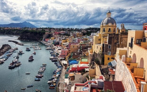 Colorful cityscape of Naples harbor with boats and historic buildings under moody clouds
