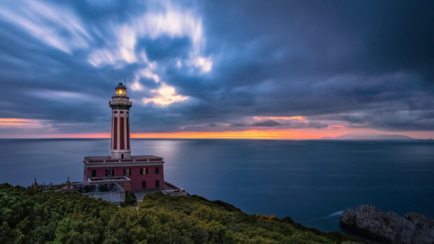 A lighthouse standing on the coast of Naples during a colorful sunset with dramatic clouds