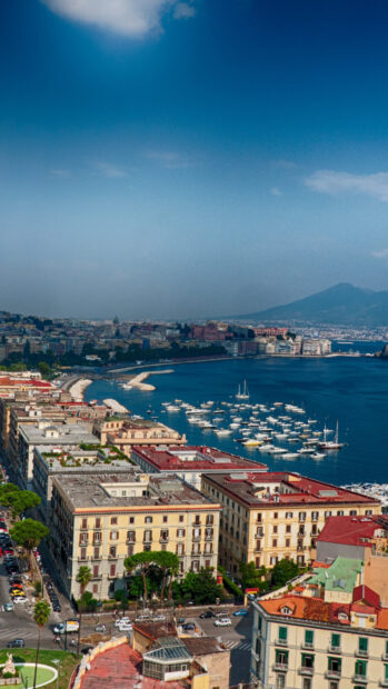 Vibrant Naples cityscape with boats in the harbor and mountain view in clear sky