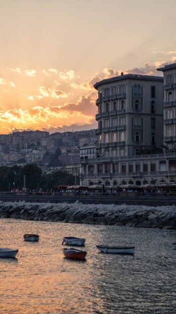 Beautiful sunset over Naples cityscape with boats floating on the calm sea water