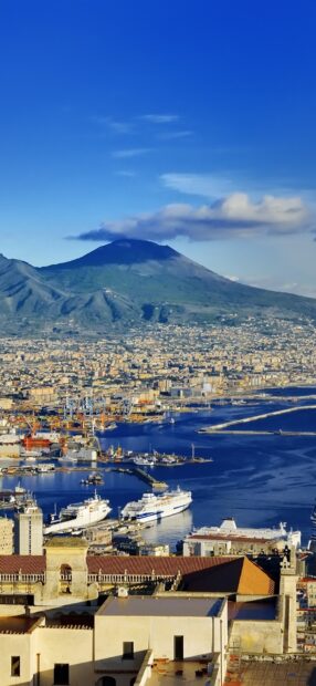 A panoramic view of Naples city with a vibrant harbor and volcano in the background