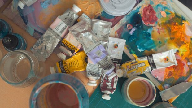 Various paint tubes and acrylic paints scattered on a creative artist workspace