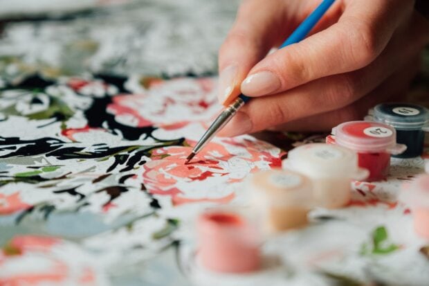 A hand painting detailed flowers on a paint by numbers canvas