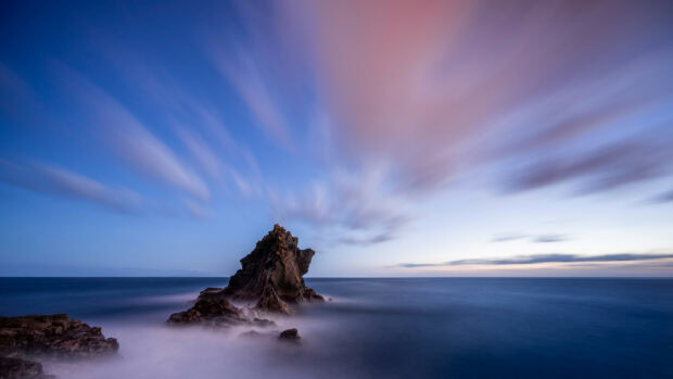 Rocky formation in Portugal sea under a colorful sky with moving clouds