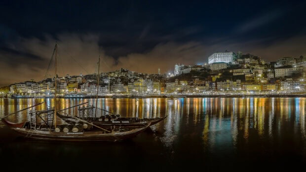 Traditional Portuguese boats floating on the river with Porto city lights at night in Portugal
