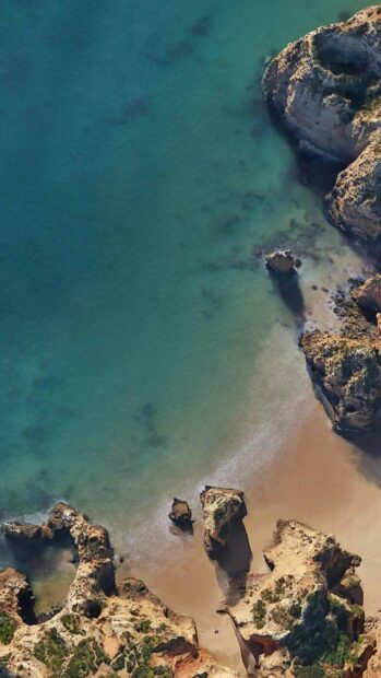 Aerial view of Portugal coastline with clear turquoise water and sandy beach surrounded by rock formations