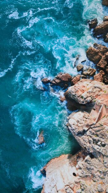 Turquoise ocean waves crashing against rocky cliffs in Portugal coastline