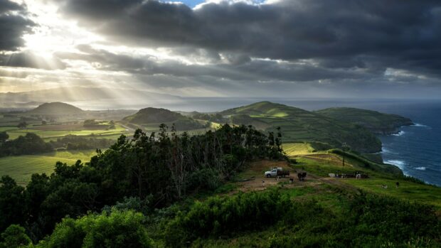 Green hills and farmland in Portugal under dramatic cloudy sky with sun rays