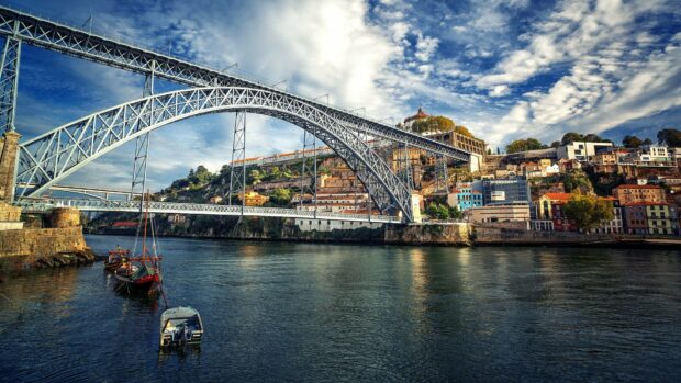 The steel arch bridge over Douro river with boats and hillside buildings in Porto Portugal