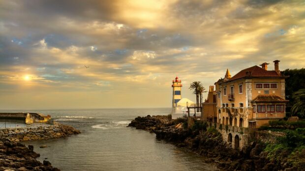 A scenic view of Portugal coastline featuring a lighthouse and historic buildings under a cloudy sky