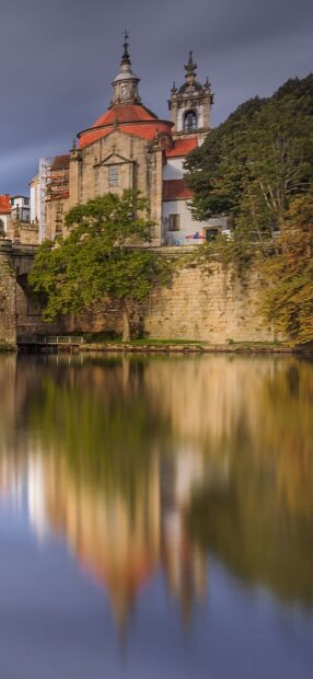 Historic Portugal architecture reflected in calm river water with surrounding trees