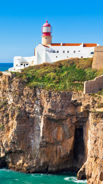 Lighthouse on cliff overlooking ocean in Portugal with clear blue sky