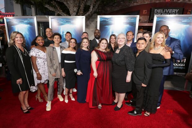 A group of people standing on a red carpet at a formal event with movie posters in the background