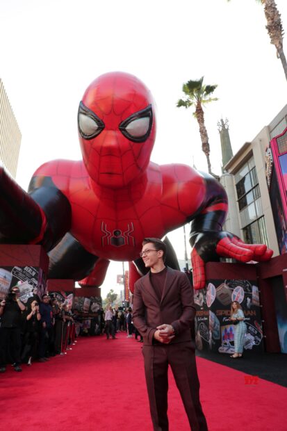 A man standing on the red carpet with a giant Spider Man figure behind at an event