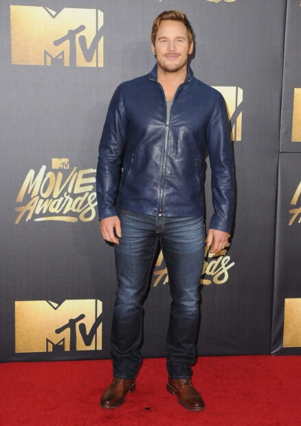 Man standing on red carpet at movie awards event wearing a blue leather jacket and jeans