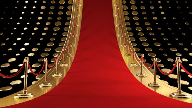 A luxurious red carpet with golden stanchions and ropes on a shiny gold floor with round decorations