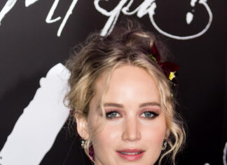 A woman wearing a white dress posing at a red carpet event with elegant makeup and hair