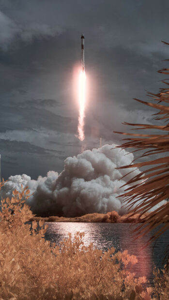 SpaceX rocket launch with smoke clouds and water reflections at sunset