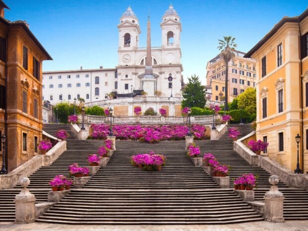 The Spanish Steps in Rome decorated with vibrant pink flowers and historic buildings in the background