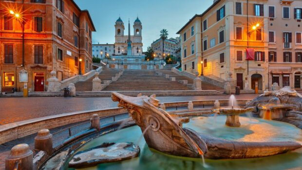 The historic Spanish Steps in Rome with a detailed fountain and surrounding buildings in the evening light