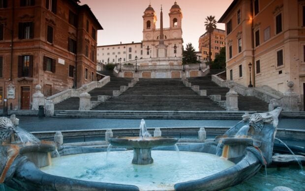 The Spanish Steps in Rome with a clear fountain in front and historic buildings surrounding the area