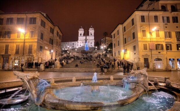 Night view of Spanish Steps with fountain and people gathered around in Rome