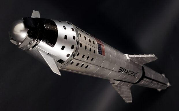 A detailed silver starship model with the SpaceX logo and American flag on the side