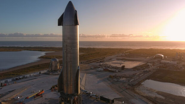 Starship standing at a launch site during sunset with ocean in the background
