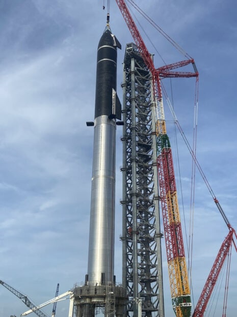 Starship rocket being lifted by a crane at the launch pad structure in clear sky