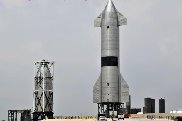 A large starship on the launch pad with another starship prototype nearby under a cloudy sky